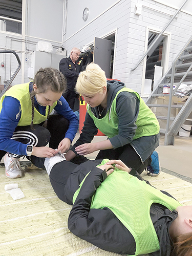 Heidi Aholainen (vas.) ja Anna Taipale auttamassa Kanerva Repoa palolaitoksen ensiapurastilla.  